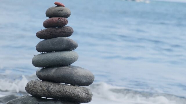 Smooth zen-like pebbles stacked in balanced pyramid against ocean waves, Balanced stones on beach, Meditation and mindfulness, harmony, travel, and serenity coastal retreats