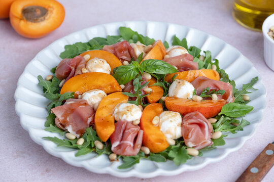 Fresh salad made with arugula, fresh peaches, prosciutto, mini mozzarella cheese, arugula, and toasted pine nuts, drizzled with balsamic glaze. Healthy dining and Mediterranean cuisine concepts.