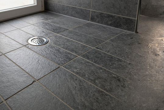 modern bathroom with sleek gray tiles and stainless steel drain near large window