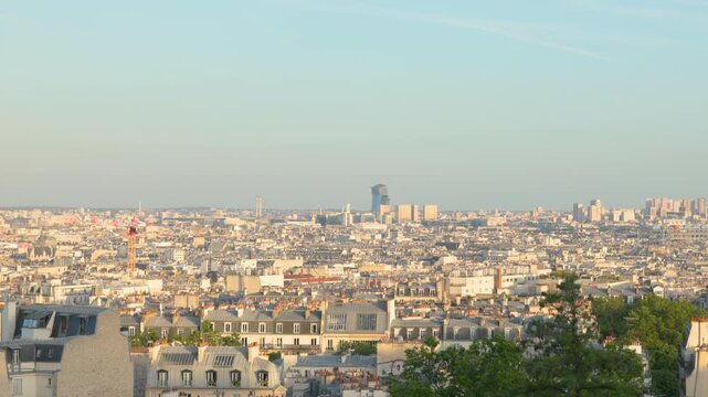 A wide panoramic shot panning across the expansive cityscape of Paris, showcasing layers of urban architecture and historic apartment rooftops under a clear bright sky.