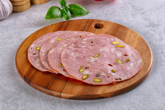 Sliced mortadella with pistachios on wooden cutting board