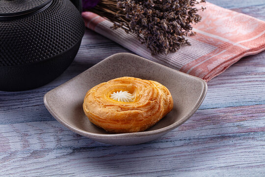 Golden danish pastry with cream filling on ceramic plate with teapot and lavender