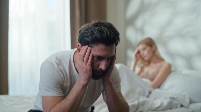 Frustrated Caucasian man husband suffering thinking separated sitting on bed with quit offended woman wife in bedroom. Couple upset with conflict partners suffer breakup intime failure family divorce