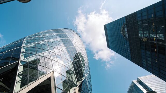 Tilting camera revealing faceted glass curved tower and glass high-rise from street, reflecting sky