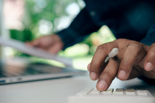 Business Professional Calculating Procurement Costs Using Calculator and Laptop at Modern Workspace with Financial Documents, Budget Planning Analysis, Purchasing Decisions, Green Natural Background