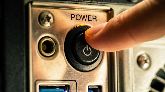 Approaching adult fingertip pressing power button on computer at desk, powering system, LED glowing