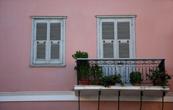 Old traditional Neoclassical house facade with a salmon pink stucco wall, grey wooden window shutters and a balcony with a handcrafted wrought iron railing in Koroni, Messinia Greece.