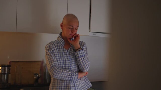 Pensive female cancer patient standing alone in kitchen during recovery journey, highlighting resilience, introspection, emotional strength and healing process