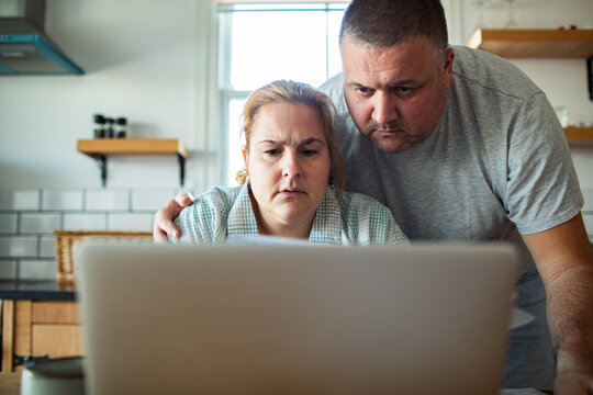 Worried middle-aged couple checking bills on a laptop in home kitchen