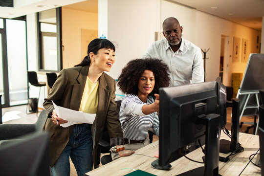 Diverse coworkers collaborating at computer in modern office
