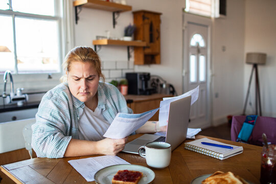 Concerned woman reviewing household bills at kitchen table