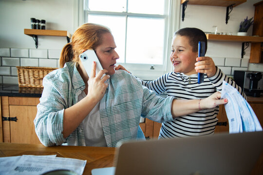 Mother on phone juggling bills with son in kitchen