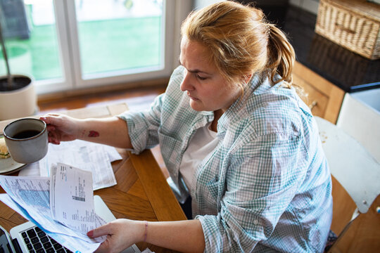 Woman paying household bills at kitchen table with coffee