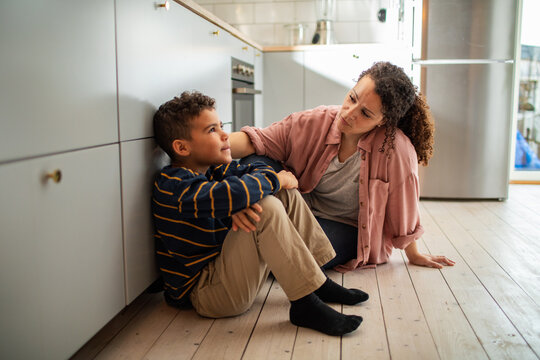 Mother comforting sad son on kitchen floor at home