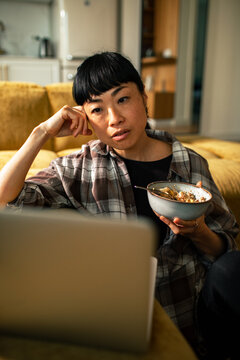 Woman eating meal while watching laptop at home