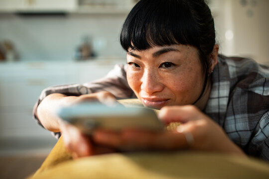 Smiling woman relaxing on sofa using smartphone at home
