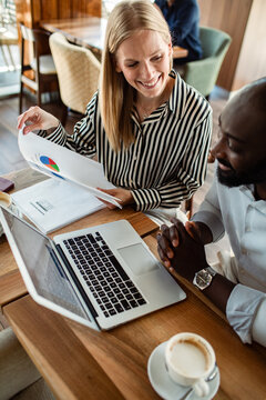Smiling coworkers reviewing sales report in cafe