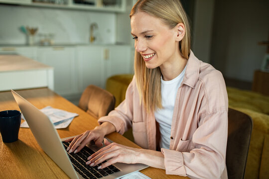 Smiling woman working on laptop in home kitchen