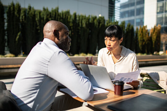 Business colleagues discussing financial report outdoors in office courtyard