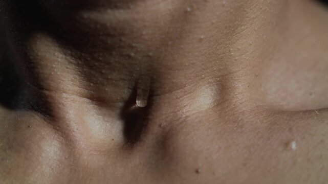 Sliding droplet over bare neck or chest in dark studio, gravity pulling, key light revealing pores
