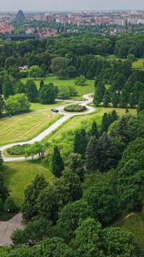 Green Urban Park Pathways People Walking Cityscape Skyline Horizon Aerial View Lifestyle. This vertical high-angle drone perspective captures a vibrant metropolitan public garden filled with lush gree