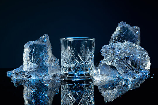 Crystal glass of vodka and ice shards against a black reflective background.