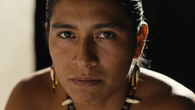Opening eyes at start barechested man holding gaze in studio with beaded drops and shell necklace
