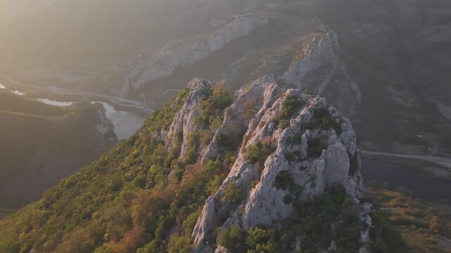 Dramatic drone semi-circle rotation showcasing a natural stone gateway on a hill top, revealing a vibrant sunset horizon. High quality 4K video.