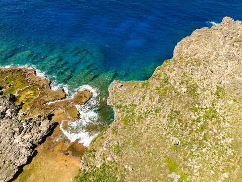 Aerial view of Chigit Beach with rugged limestone cliffs, turquoise coastal waters, and lush green vegetation in Northern Tinian, Tinian, Northern Mariana Islands.
