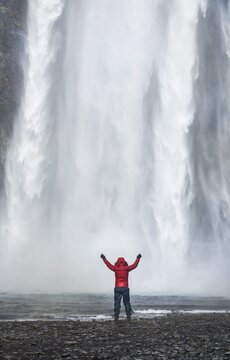 Hiker with arms outstretched in front of Sk&oacute;gafoss Waterfall in winter, Sk&oacute;gar, Southern Region, Iceland