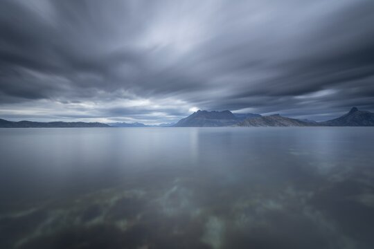 The Vestfjord in Nordland, Norway, near Bod&oslash;, impresses with a dramatic atmosphere. Dark clouds sweep across the water and create a mystical atmosphere. The rugged cliffs and majestic mountains are reflected in the tranquil fjord and provide an impressive backdrop