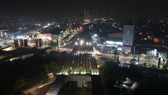 Aerial view of the illuminated elevated highway construction and urban landscape at night in Bekasi Barat, West Java, Indonesia.