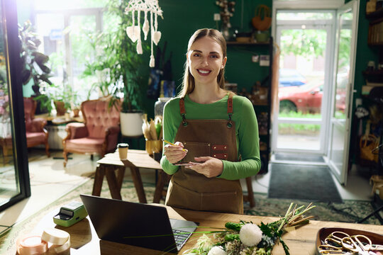 Portrait of young adult Caucasian woman florist holding notepad while managing flower shop orders. Ideal for small business, retail technology, ecommerce content