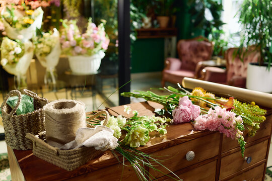 Close up of florist workspace displaying cut flowers, wrapping paper, twine, baskets in flower shop, supporting bouquet making and retail branding for floral business