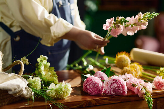 Close up of florist arranging fresh flowers on worktable, preparing bouquet for retail sale and event decor. Ideal for floral business marketing, handmade product branding, small shop promotion