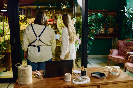 Back view of women selecting flower arrangements in florist shop, discussing purchase and retail service. Useful for small business marketing, local commerce, customer experience