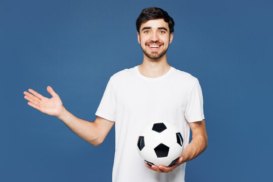 Young shocked surprised fun overjoyed man fan wear basic white t-shirt cheer up support football sport team hold in hand soccer ball watch tv live stream look camera isolated on plain blue background.