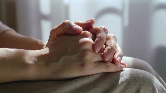 Shifting adult hands interlacing and releasing fingers on light lap covering, adjusting for comfort