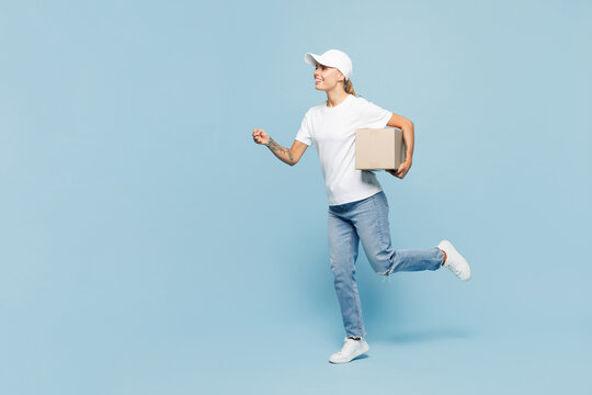Full body delivery employee young woman wear white cap T-shirt uniform workwear work as dealer courier hold in hand cardboard box isolated on plain pastel light blue background studio Service concept