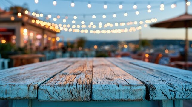 Empty, weathered wooden table on patio at dusk with glowing string lights