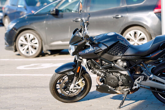 Minsk, Belarus. Jun 18, 2026. Aprilia Shiver 750 side view of black naked sports motorcycle parked on paved tile stone parking lot next to passenger vehicles during bright sunny daytime
