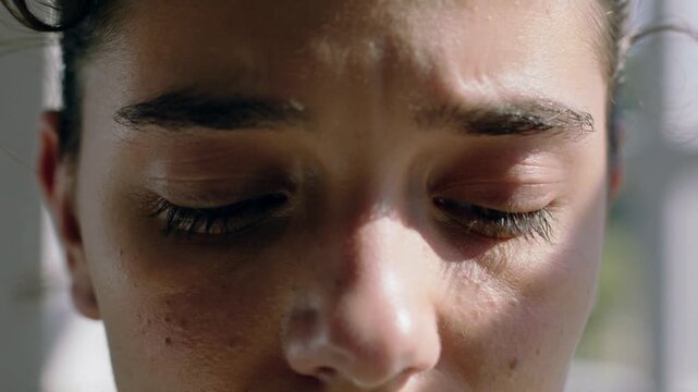 Blinking adult woman closing eyes slowly in room with vertical blinds, reacting to bright sunlight