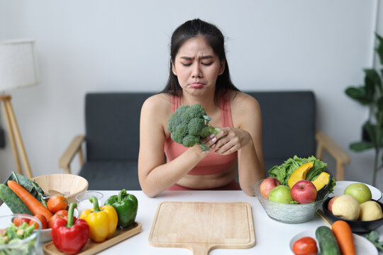 Young woman disliking broccoli while preparing healthy food.