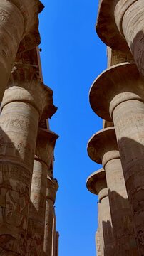 Karnak Temple in Luxor, Egypt. Massive hieroglyphic columns in Great Hypostyle Hall, Karnak Temple Luxor Egypt. Upward view of ancient carved pillars against blue sky.