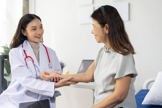 Asian female doctor examining an elderly patient's hand during a medical consultation, health care, and diagnosis in a clinic.