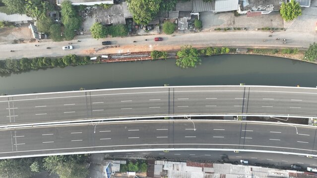 Aerial view of an elevated highway spanning over a river with surrounding urban infrastructure, Bekasi Barat, West Java, Indonesia.