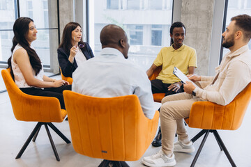Naklejka premium Diverse group of people sitting in a circle during a support meeting, communicating and sharing ideas