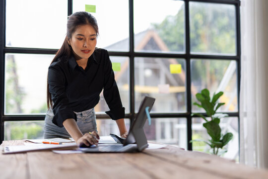 Asian businesswoman examining paperwork and a digital tablet, working on business strategy in a office.