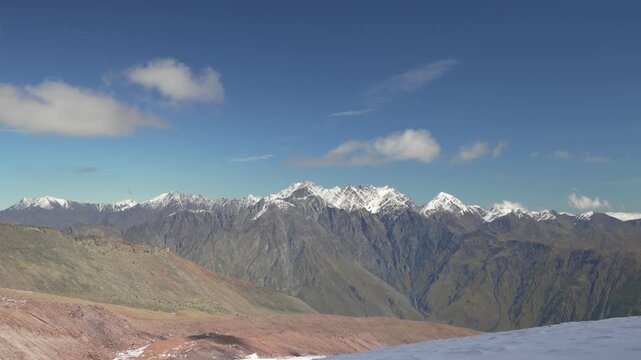 4K mountain landscape with slowly moving clouds over snowy peaks and blue sky.