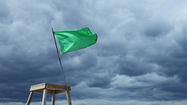 The scene shows a green flag flying on a wooden post against a backdrop of dark clouds in the evening sky. The setting appears open with no people present.